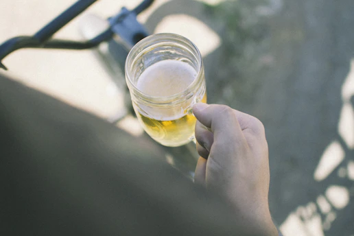 A close-up shot of a member holding a frothy homebrewed beer in a rustic mason jar at a mash club gathering.