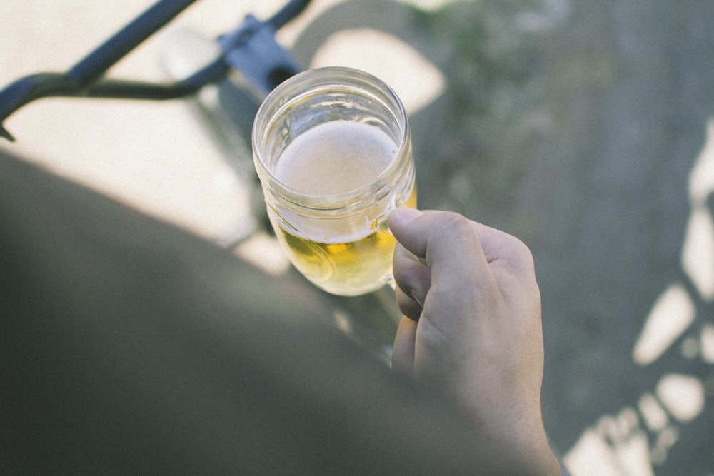 person holding clear glass mason mug