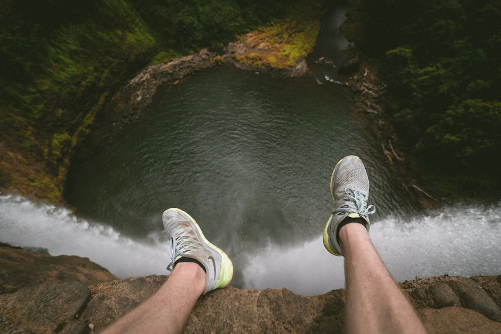 person sitting on edge of mountain overlooking lake during daytime