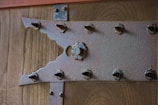 A close-up of a wooden surface with a textured metallic bracket featuring an intricate design and several protruding bolt heads.