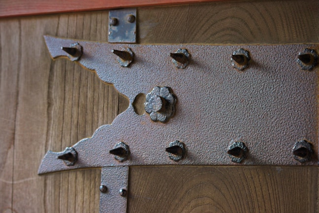 A close-up of a wooden surface with a textured metallic bracket featuring an intricate design and several protruding bolt heads.