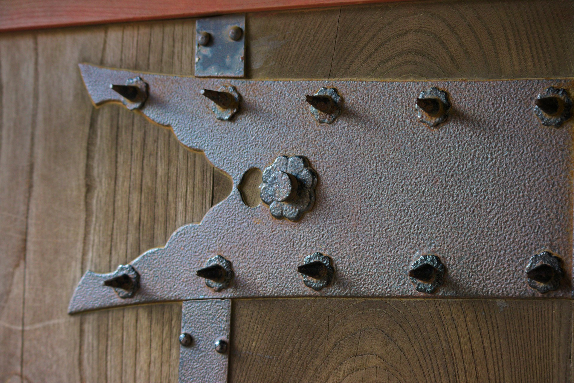 A close-up of a wooden surface with a textured metallic bracket featuring an intricate design and several protruding bolt heads.