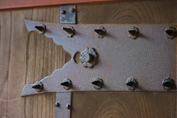 A close-up of a wooden surface with a textured metallic bracket featuring an intricate design and several protruding bolt heads.