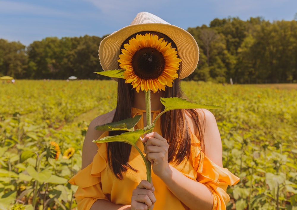 mujer sosteniendo cubriendo su cara con girasol en el campo cerca de los árboles durante el día