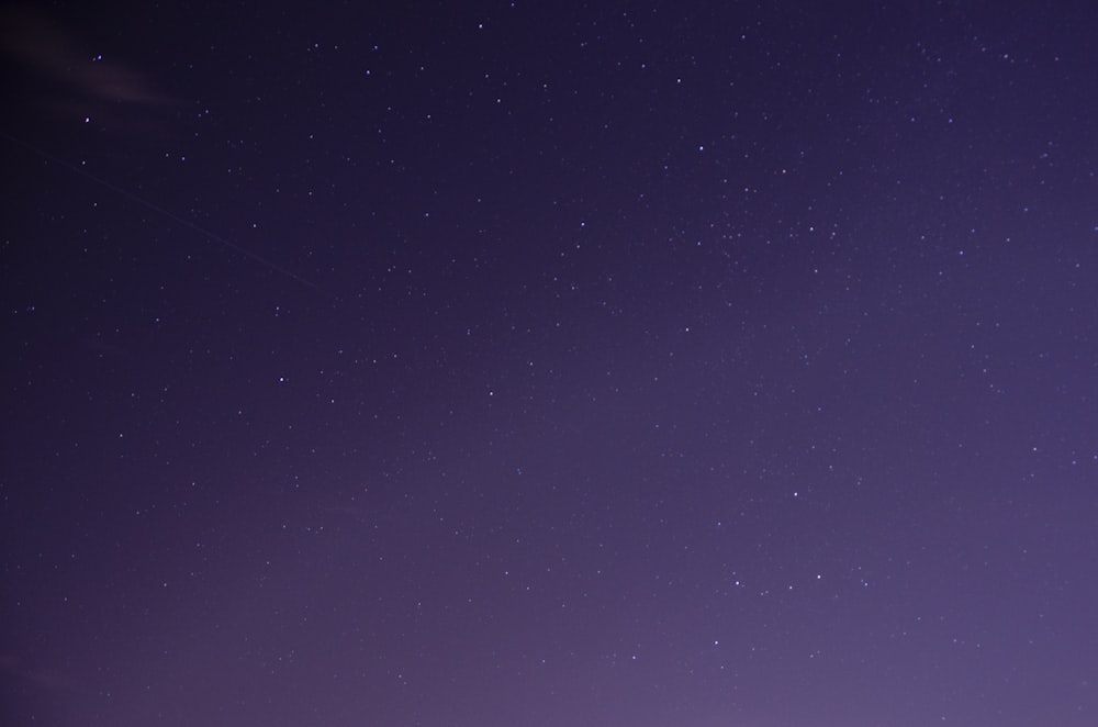 a night sky with stars and a plane in the distance