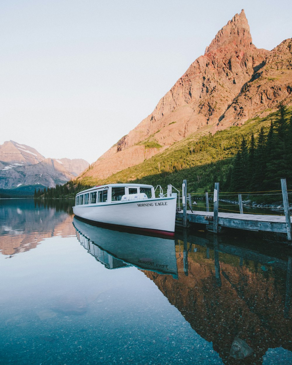 white and red boat on body of water near brown mountain