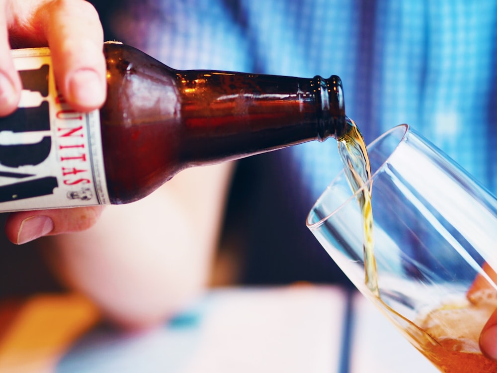 person holding amber glass bottle pouring liquid on drinking cup