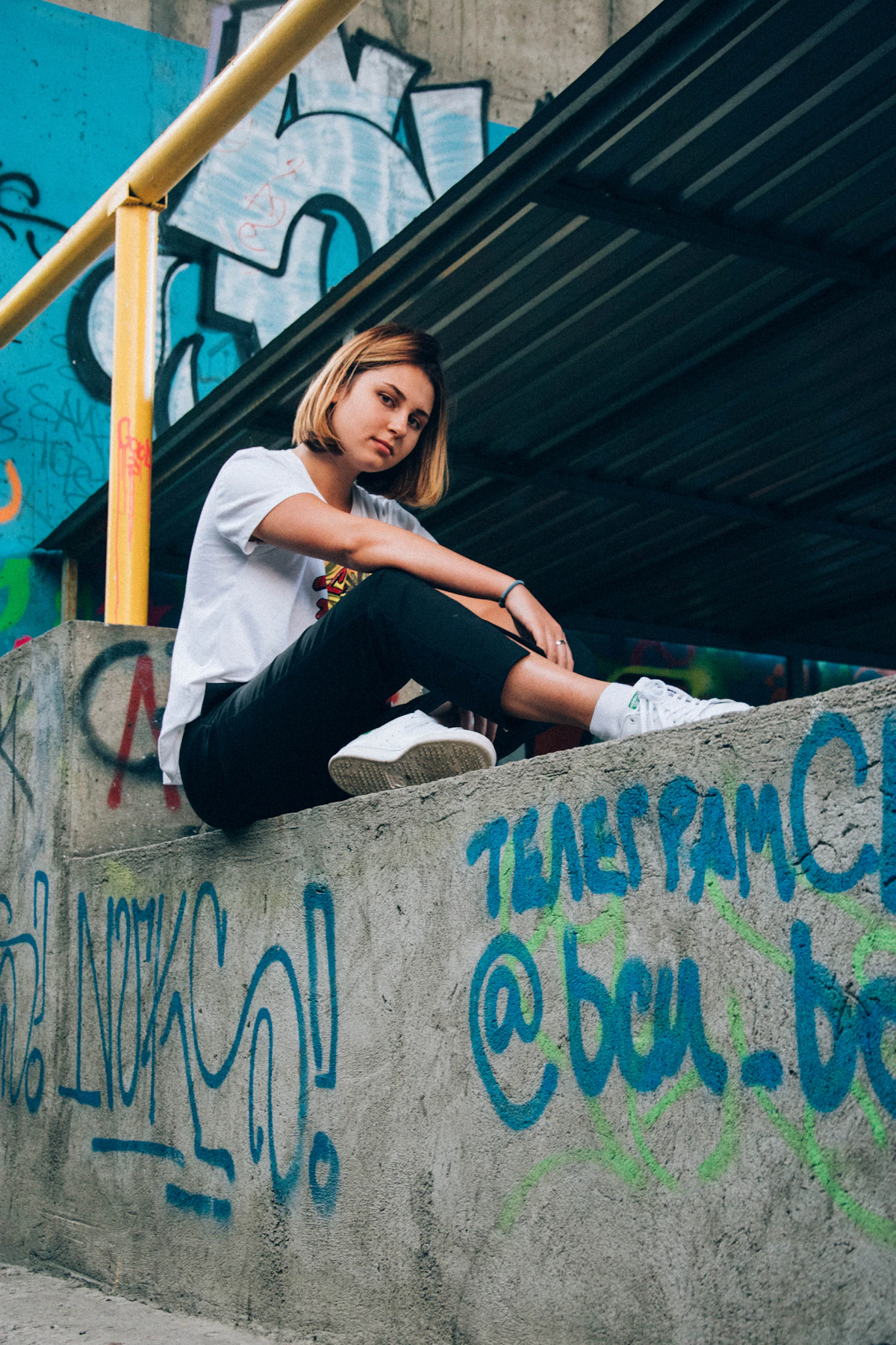 Chica adolescente sentada frente a una vibrante pared de graffiti, relajada y libre