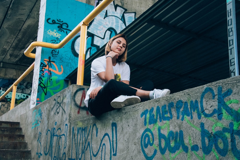 Femme vêtue d’une chemise blanche et d’un pantalon noir assise sur un rail en béton