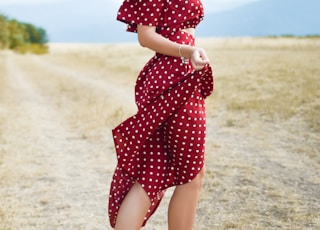 woman in red polka-dot dress standing in the middle of grass field during daytime