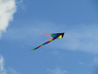 A colorful kite soaring high against a bright blue sky with soft clouds.