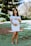 maternity photography of woman in white and blue pinstripe off-shoulder mini dress standing on green grass