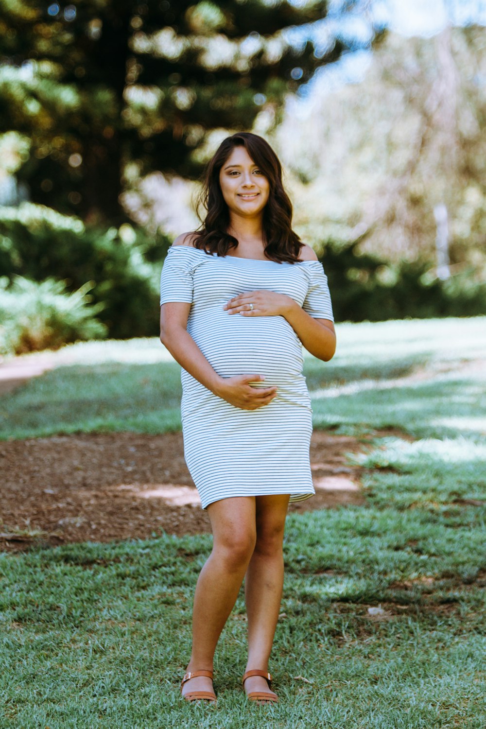 fotografia di maternità di donna in mini abito bianco e blu gessato con spalle scoperte in piedi sull'erba verde