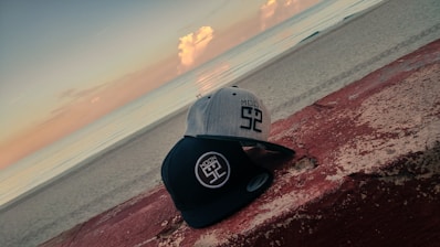 A close-up of a stylish cap embroidered with a wave logo, resting on driftwood.