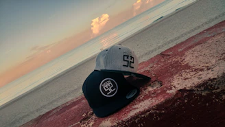 A close-up of stylish caps with embroidered fishing logos resting on a rocky shore.