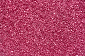 A densely packed collection of small, pink granules that resemble sugar crystals. The surface texture appears rough due to the numerous tiny, faceted particles reflecting light.