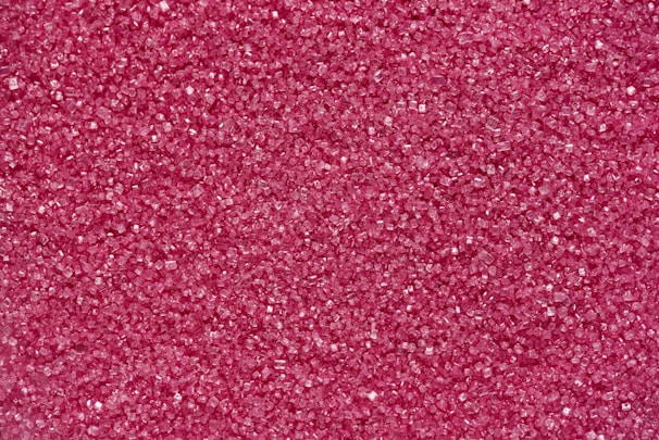 A densely packed collection of small, pink granules that resemble sugar crystals. The surface texture appears rough due to the numerous tiny, faceted particles reflecting light.
