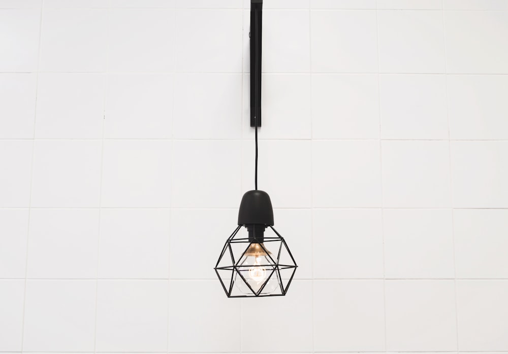 Single geometric lantern with light bulb hanging on a white wall