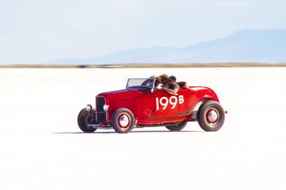 an old red car driving on a flat plain