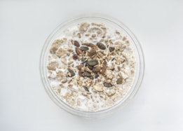 A bowl filled with milk and topped with various grains, seeds, and nuts. The mixture appears to include oats, pumpkin seeds, and possibly pieces of dried fruit.
