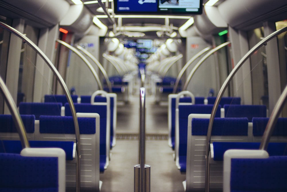An empty train with blue seats and circular hand rails and monitors