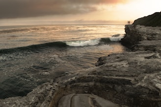 A dramatic cliffside overlooking crashing ocean waves at sunset.