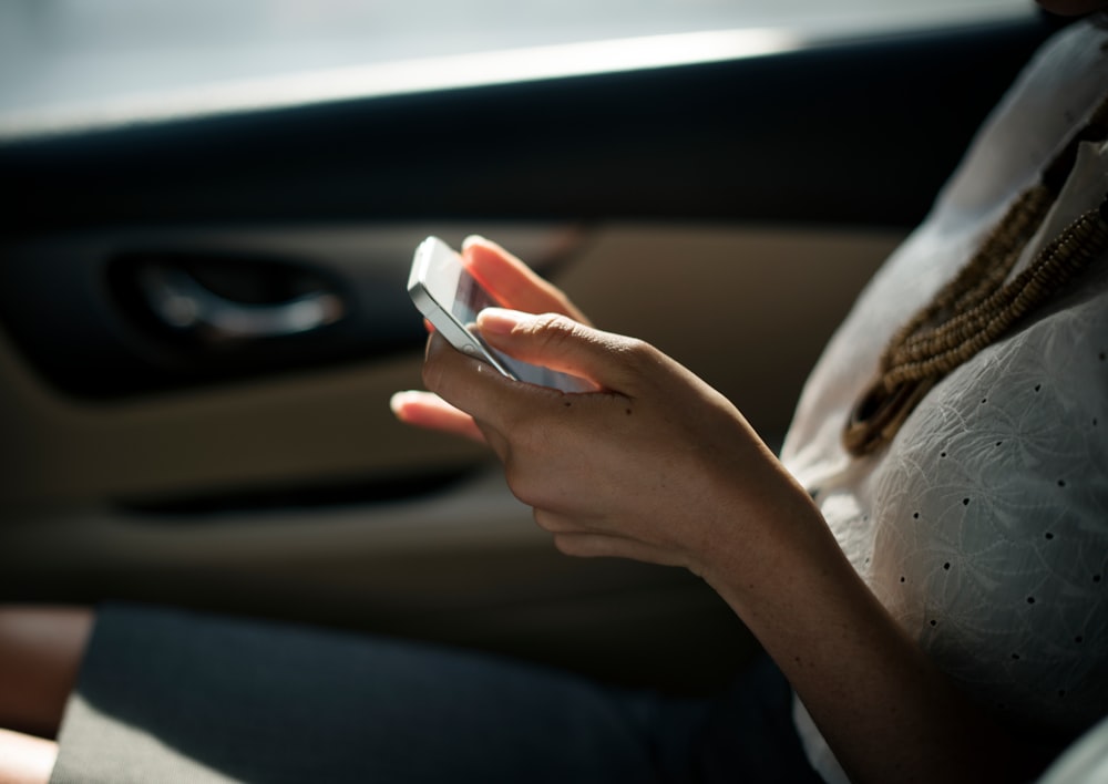 Woman sitting in car in the sunlight with a smartphone in her hands