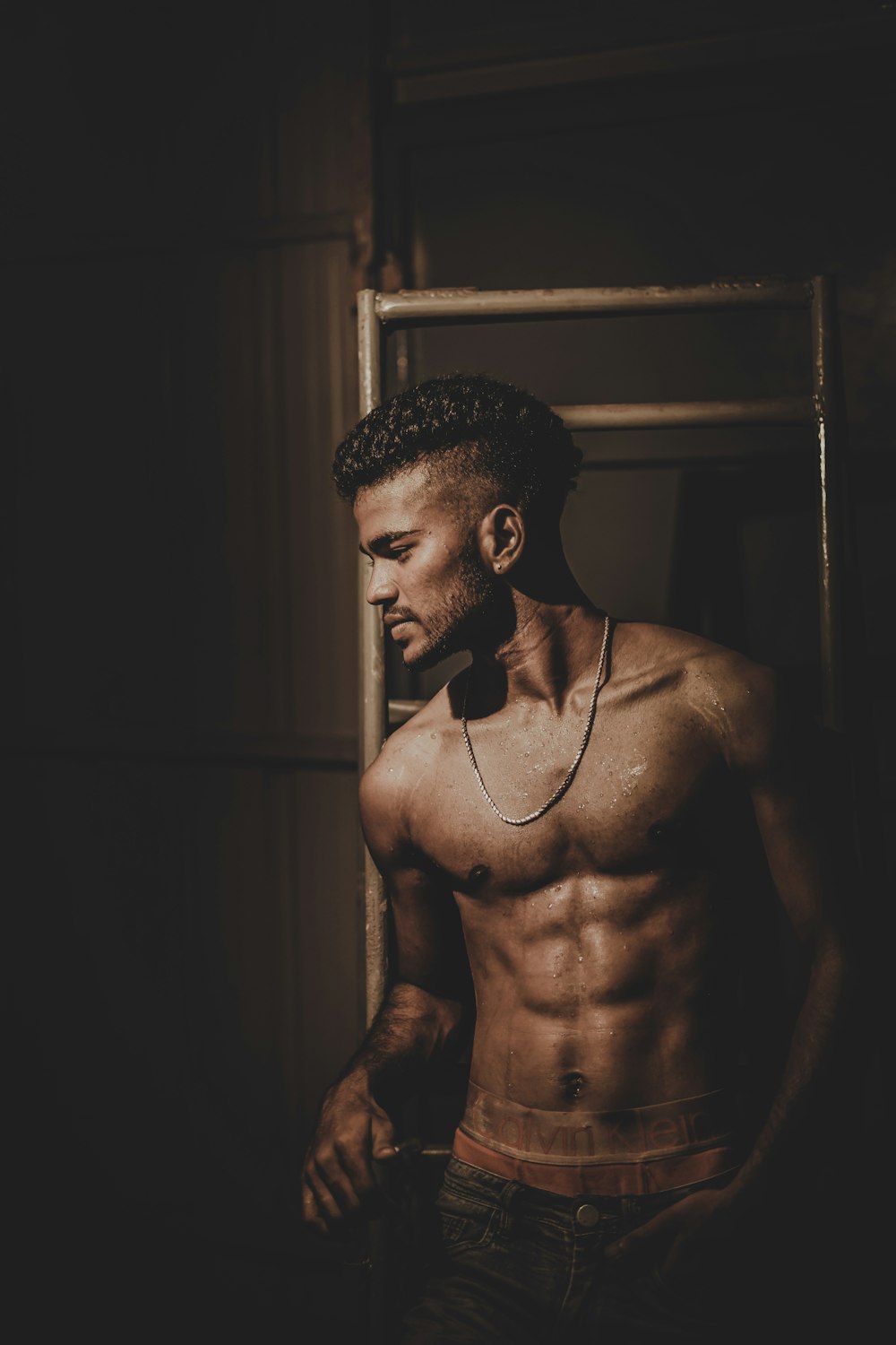 topless man wearing necklace while leaning against rack