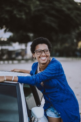 A happy gig worker standing next to their car wrapped with a colorful advertisement, smiling at the camera.