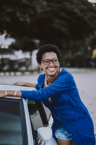 A smiling driving instructor standing beside a car with a Cardiff cityscape in the background.