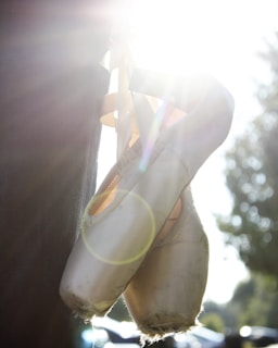 Close-up of well-used ballet shoes resting on a wooden floor with sunlight streaming in.