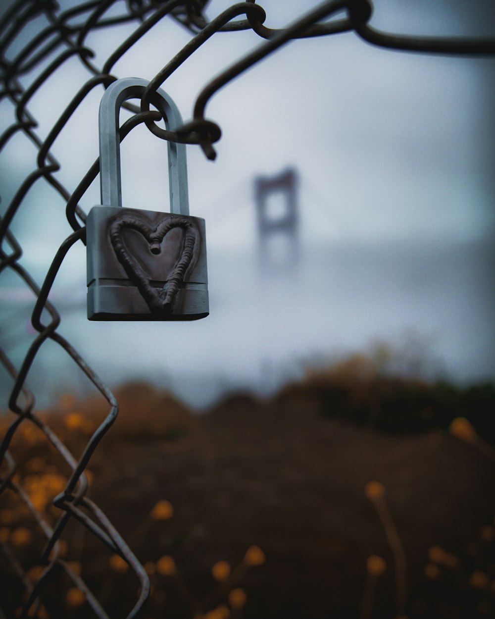 A lock on a fence with a heart etched in.