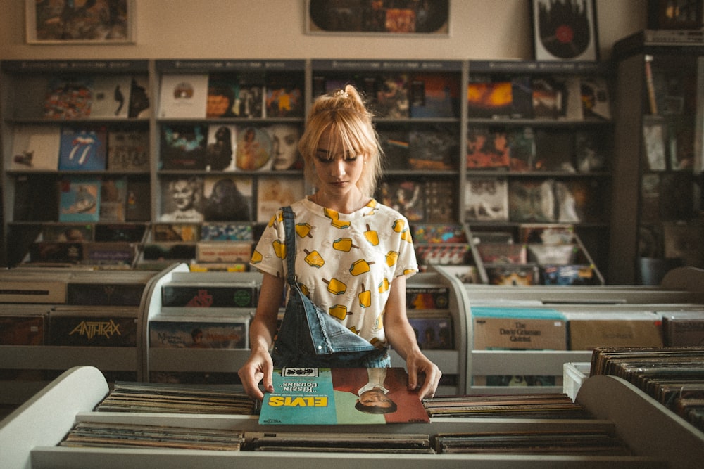 A young blonde woman looking at Elvis Presley's vinyl record in a record store