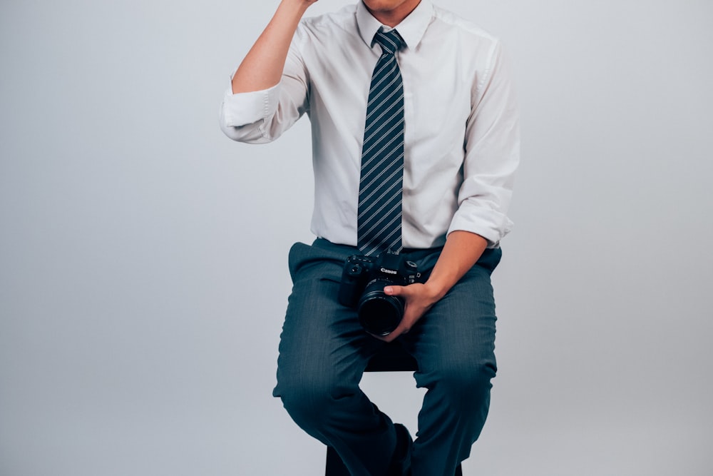 man in white dress shirt and blue pants holding DSLR camera