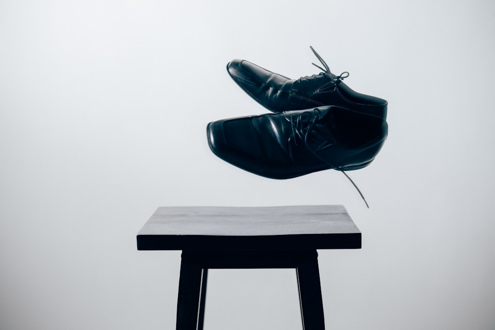 par de zapatos de vestir de cuero negro sobre mesa de madera marrón