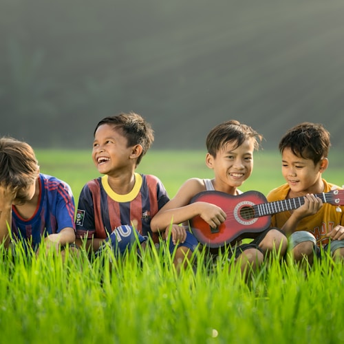 four boys laughing and sitting on grass during daytime