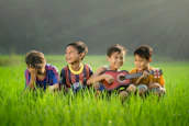 four boys laughing and sitting on grass during daytime