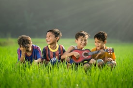four boys laughing and sitting on grass during daytime