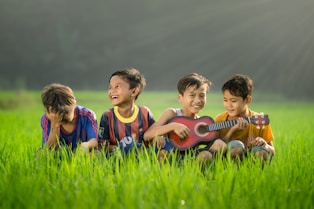 four boys laughing and sitting on grass during daytime