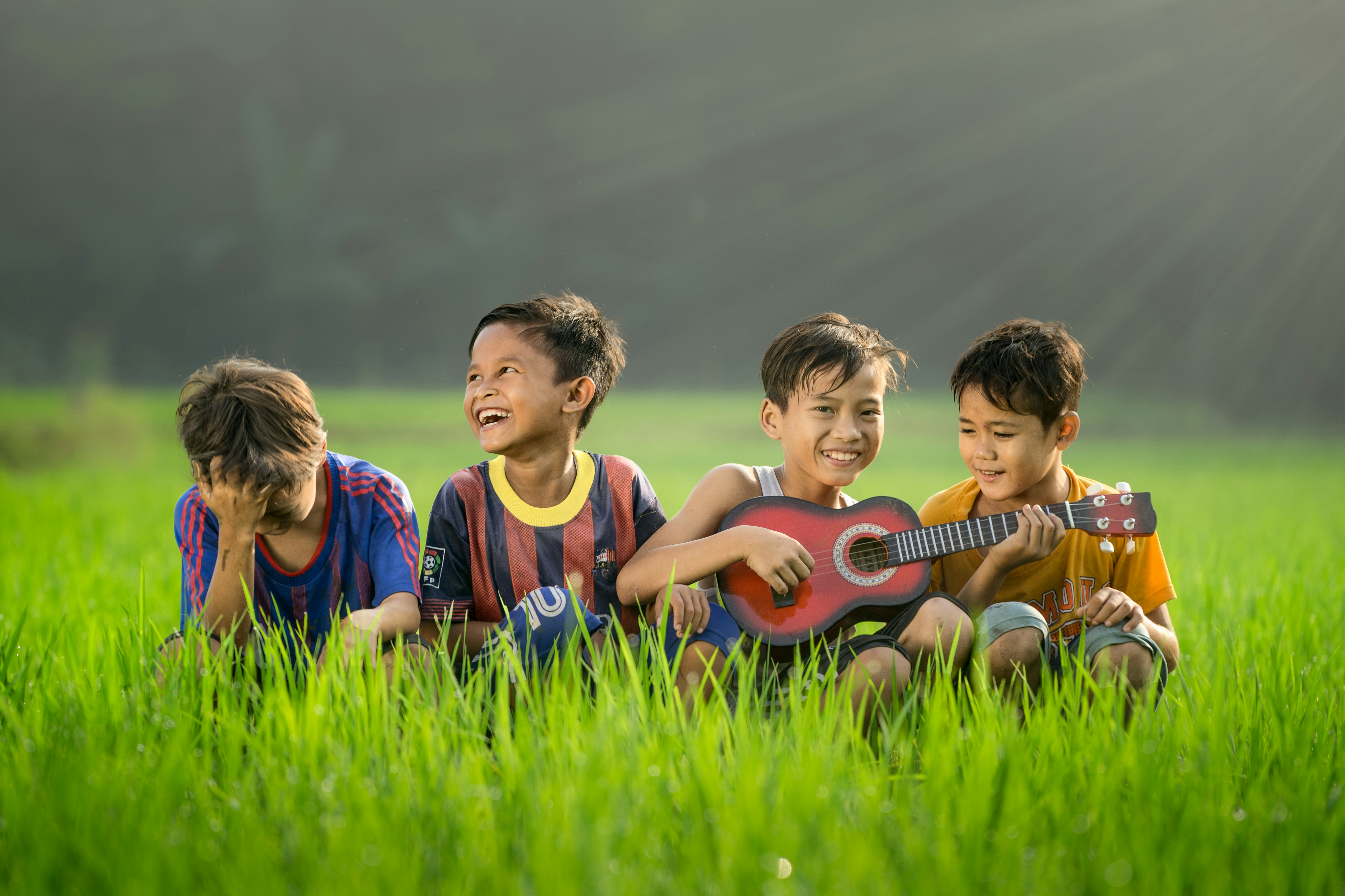 four boys laughing and sitting on grass during daytime