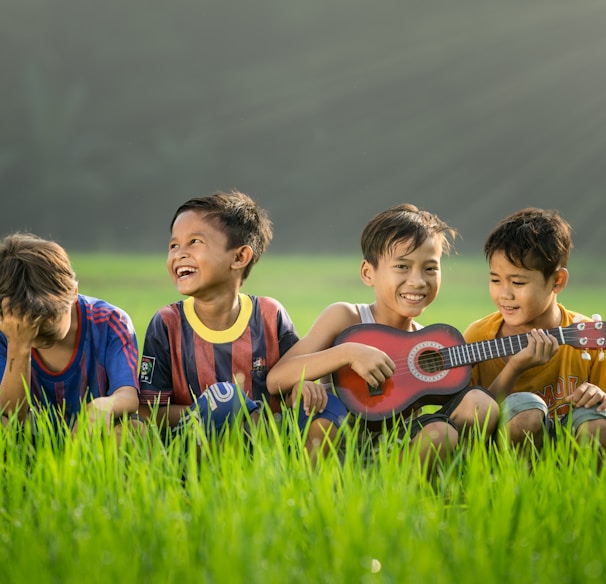 four boys laughing and sitting on grass during daytime
