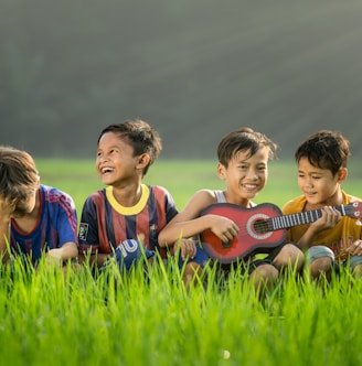 four boys laughing and sitting on grass during daytime