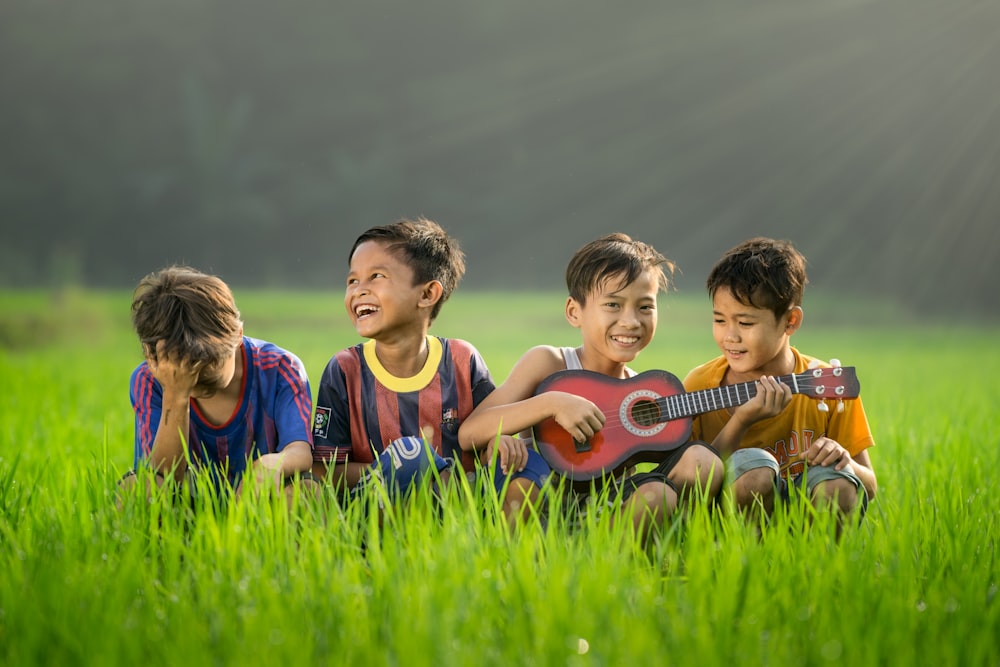 four boys laughing and sitting on grass during daytime