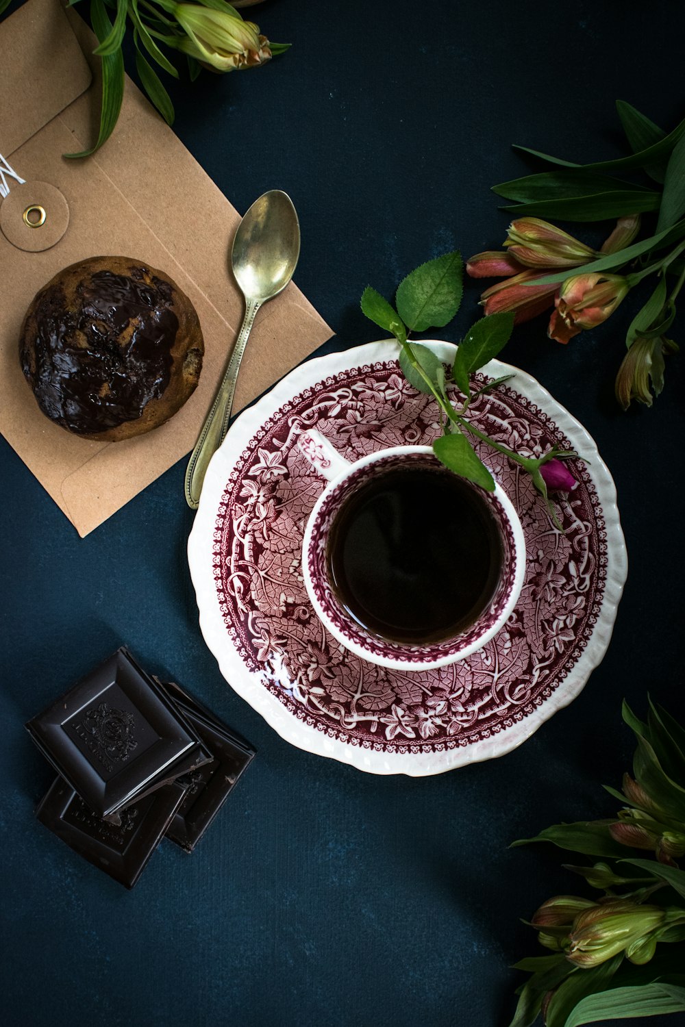 café servido em copo de cerâmica branca e vermelha ao lado de cupcake de chocolate