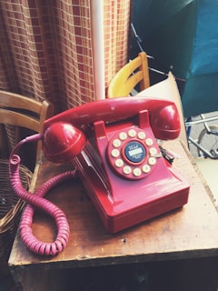 A red telephone sitting on top of a wooden table