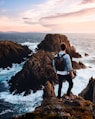man standing near cliff looking at body of water during daytime