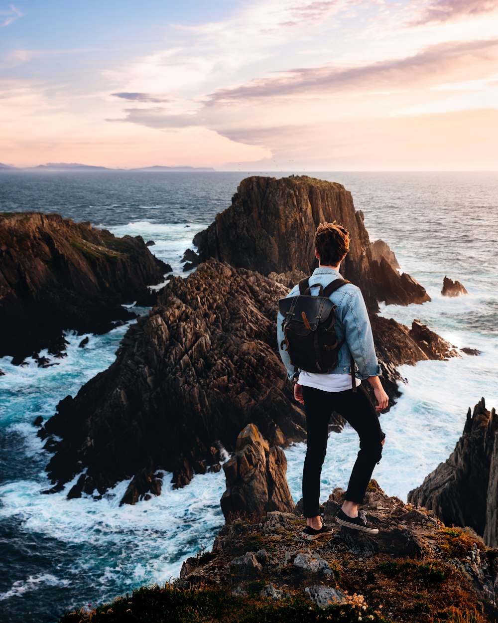 man standing near cliff looking at body of water during daytime