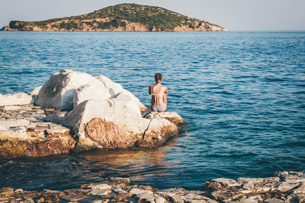 woman sitting on brown stone near body of water