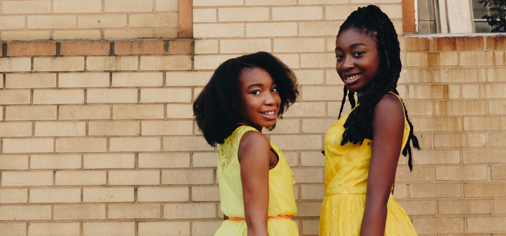 two women wearing yellow sleeveless dresses near brown brick