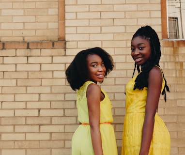 two women wearing yellow sleeveless dresses near brown brick
